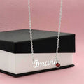 Personalized silver name necklace with red birthstone charm draped over a gift box